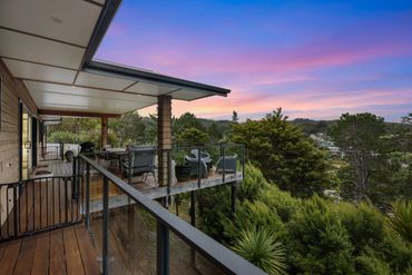 Scenic wooden balcony with chairs overlooking lush greenery at sunset.