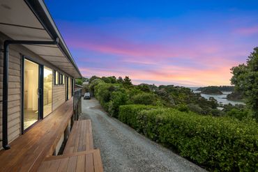 Sunset view from a wooden house balcony overlooking lush greenery and water.