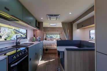 Interior of a modern camper van with kitchen, seating, and bed area.