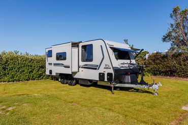 A Jayco Discovery caravan parked on a grassy field under a clear blue sky.