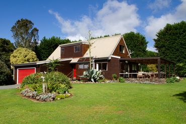 A charming wooden house with a red garage door and lush green garden.