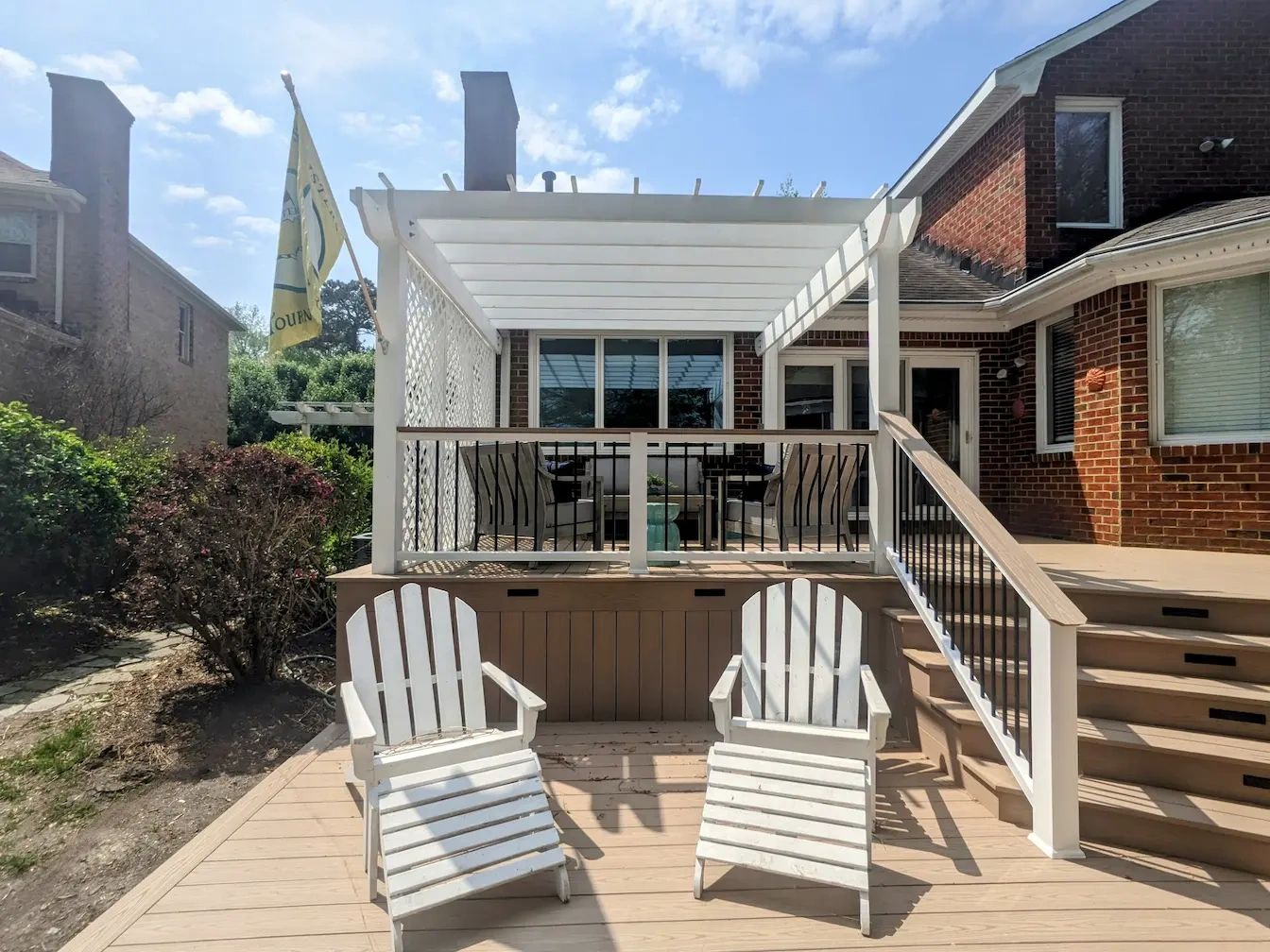 Chairs in front of a white pergola with black and white railings and PVC decking