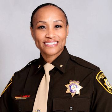 Smiling female police officer in uniform with badges and insignia.
