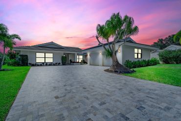 Modern single-story house with a large driveway and palm trees at sunset.