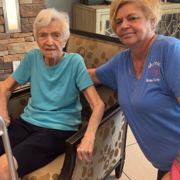 Elderly woman sitting with a caregiver in a home care setting.