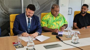 Two men signing documents at a conference table.