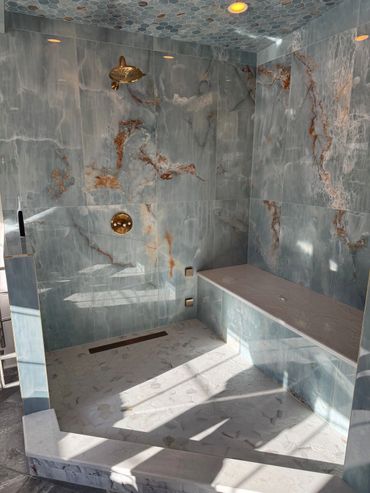Luxurious marble shower with gold fixtures and a built-in bench.