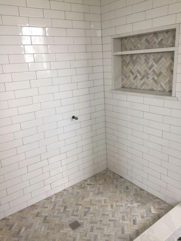 Clean white subway tile shower with herringbone floor and inset shelving.