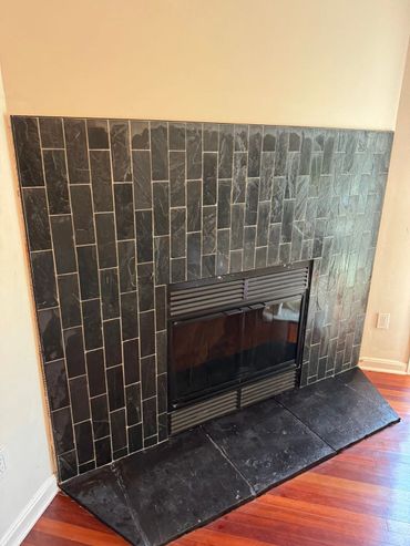Modern fireplace with black slate tiles and wooden floor.