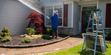 Person pressure washing a house exterior on a sunny day.