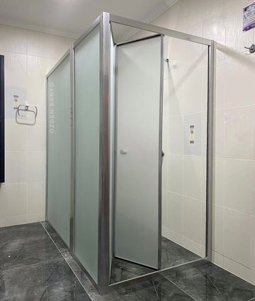 Modern bathroom stall with frosted glass and metal frames in a tiled room.