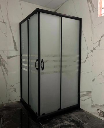 Frosted glass shower enclosure with black frame in a marble bathroom.