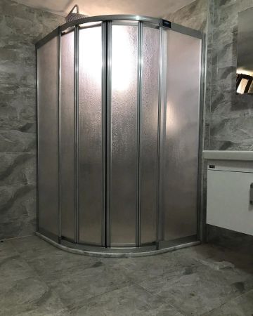 Corner shower stall with frosted glass and metal frame in a gray tiled bathroom.