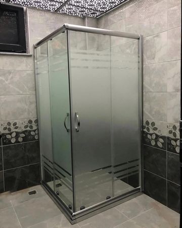 Modern glass shower enclosure with frosted and clear panels in a tiled bathroom.