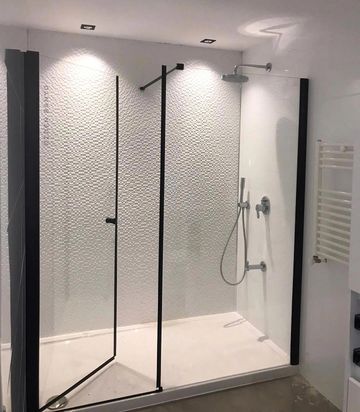 Modern walk-in shower with textured white wall and black trim glass panels.