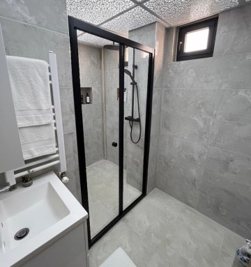 Modern bathroom with a black-framed glass shower enclosure and gray tiles.