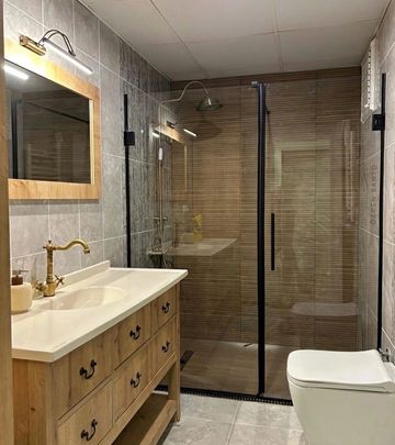 Modern bathroom with wooden vanity and glass shower enclosure.