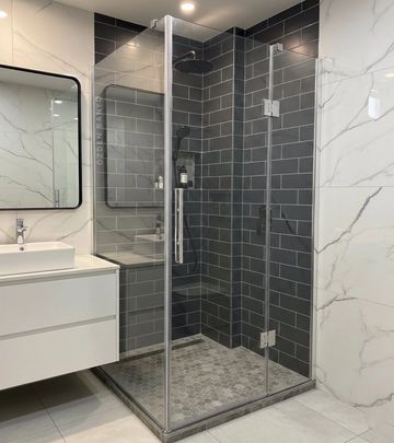 Modern bathroom with glass shower and dark tiled walls.