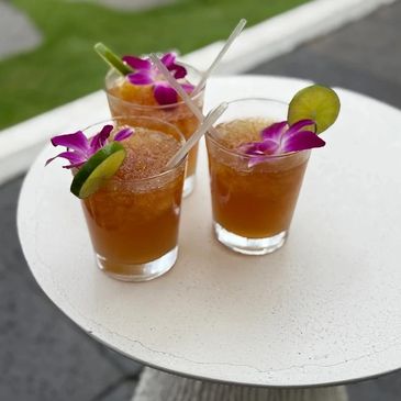 Three tropical cocktails garnished with flowers and lime on a white table.