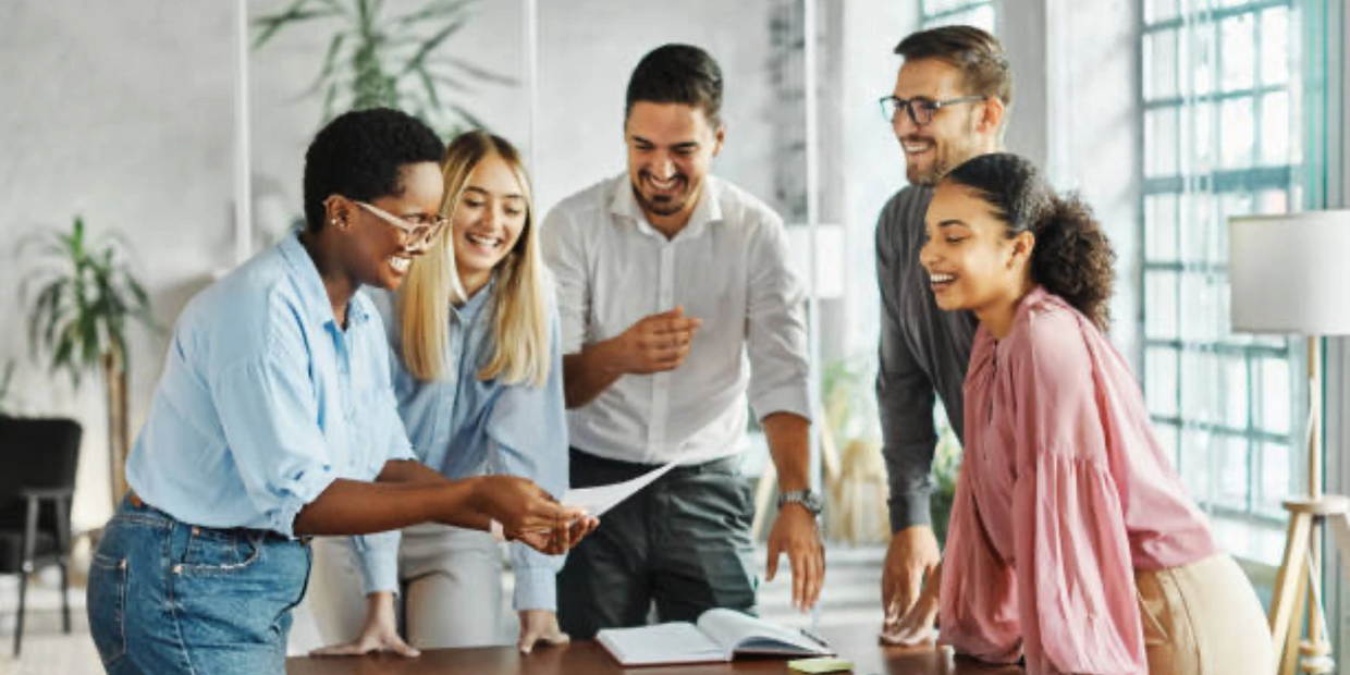 A diverse group of coworkers happily collaborating around a table in a bright office.