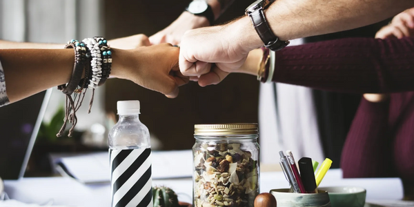 Four people fist bumping over a table with snacks and a water bottle.