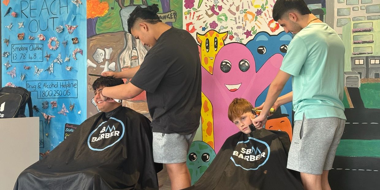 Two barbers cutting hair in a colorful room.