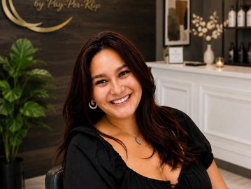 Smiling woman with dark hair seated indoors in a stylish setting.