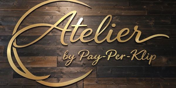 Elegant gold sign reading 'Atelier by Pay-Per-Klip' on dark wood background.