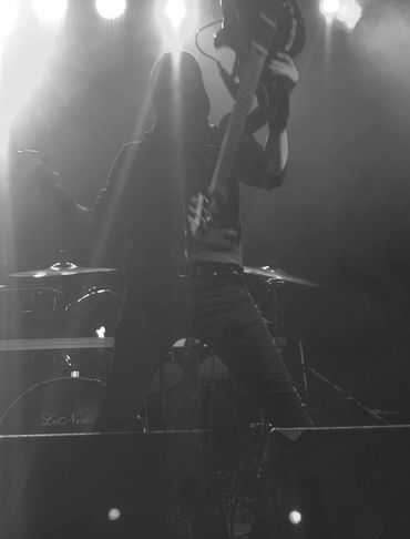 Guitarist performing energetically on a blue-lit stage with drums in the background.