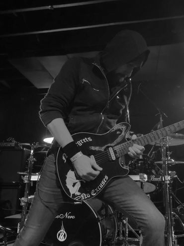 Guitarist in a hoodie playing on stage under blue and purple lights.