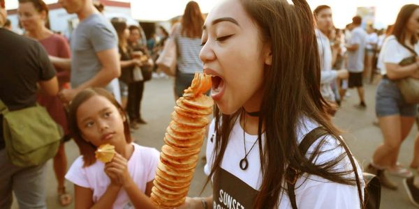 A woman enjoys a large spiral potato snack at an outdoor event.