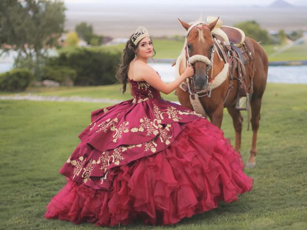 Young woman in a red floral ball gown with a horse outdoors.