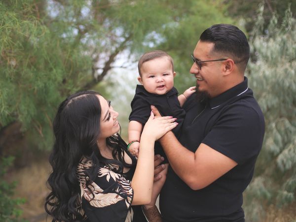 Happy family outdoors with parents holding their smiling baby.