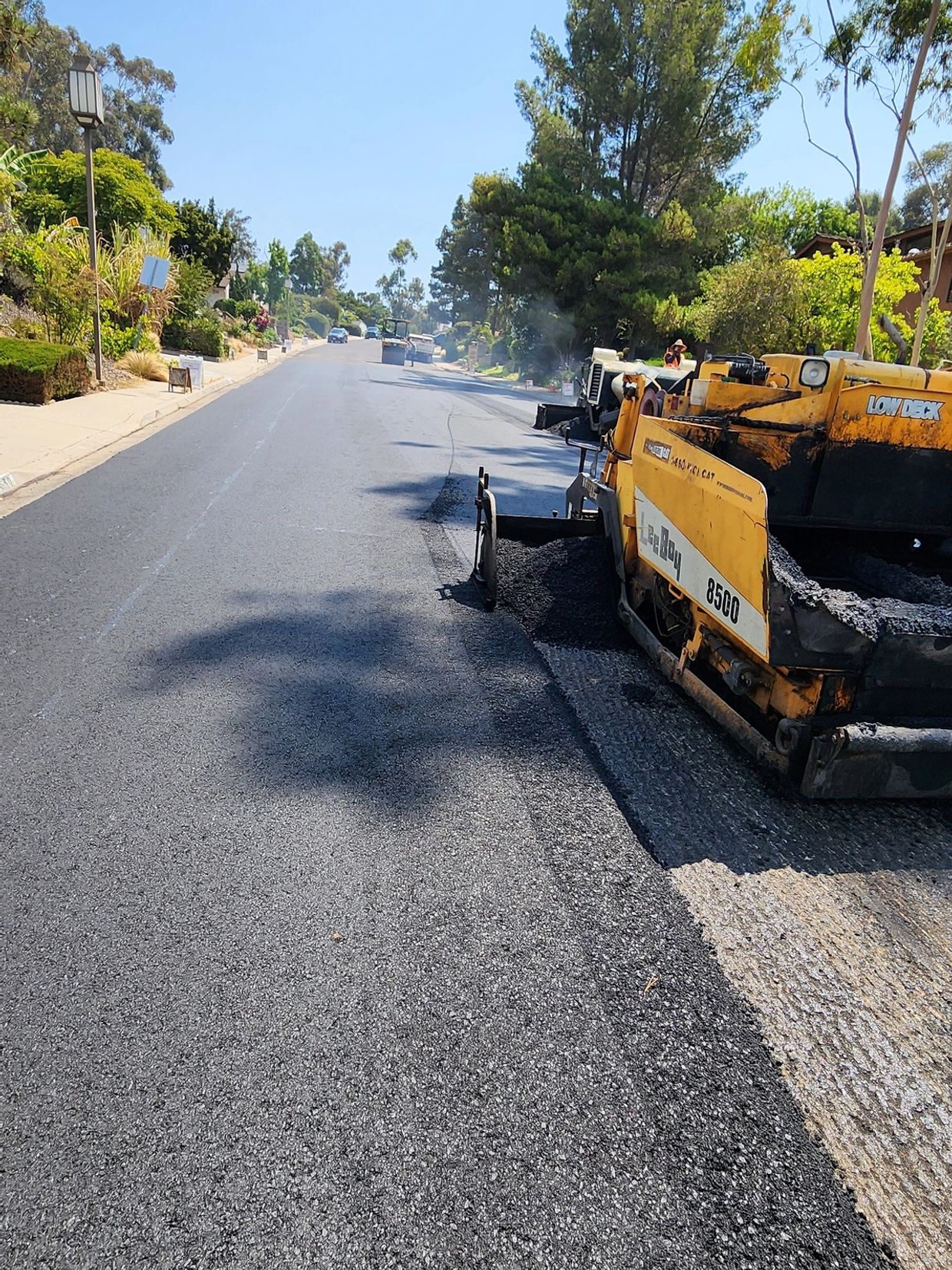 A road paving machine laying fresh asphalt on a sunny street.
