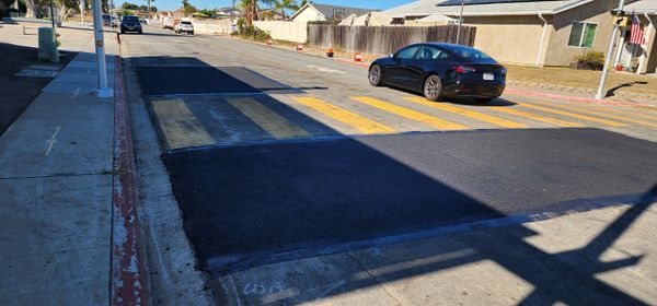 A street with a newly paved section covering a faded crosswalk.