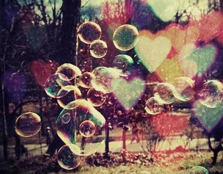 A magical photo of bubbles and hearts floating in the sky in front of a tree lined landscape