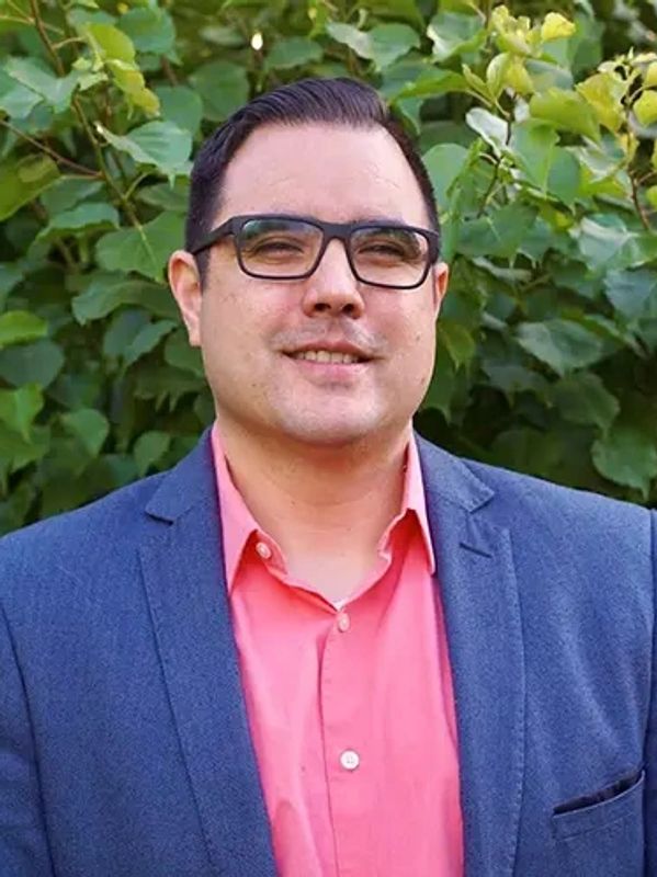 A man in glasses and a blue blazer with a pink shirt
