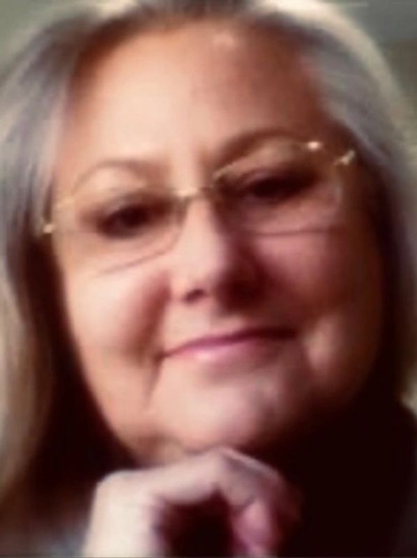 Elderly woman with long gray hair, glasses, and a gentle smile
