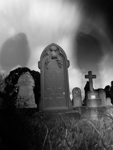 Black and white photo of old gravestones under spooky sky.
