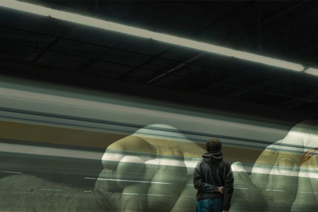 A person watches a train with a large hand mural in the background.