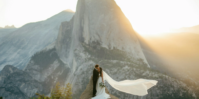 A couple shares a romantic moment on a mountaintop at sunset.
