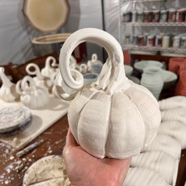 Hand holding a white clay pumpkin sculpture.