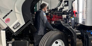 Mechanic inspecting a truck with its cabin tilted forward in a workshop.