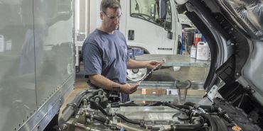 A mechanic inspecting parts near a truck engine inside a garage.