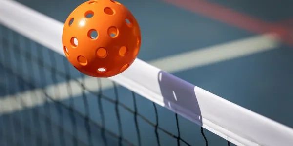 Picture of an orange  pickleball sailing over a pickleball net.