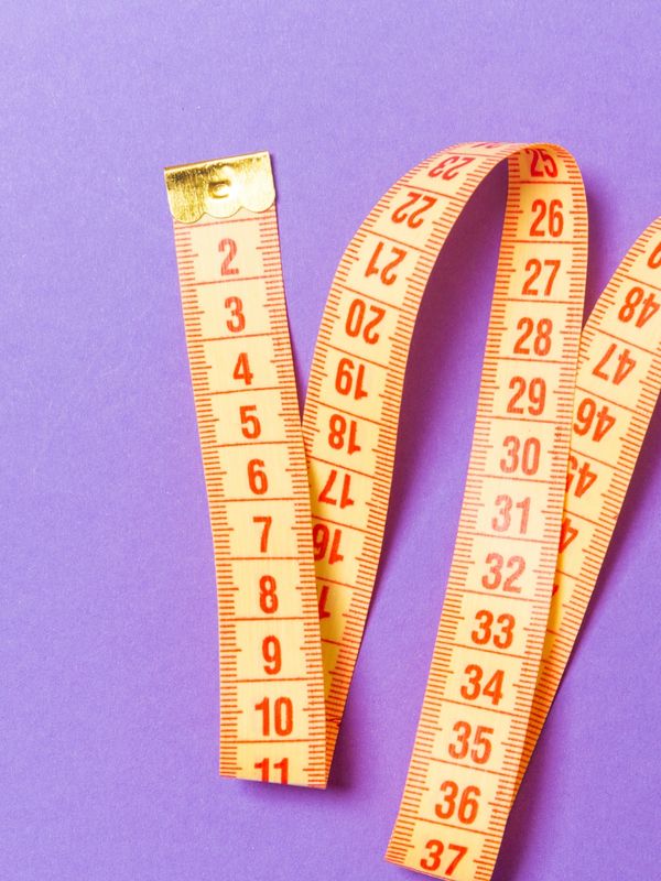 A yellow measuring tape with red numbers on a purple background.