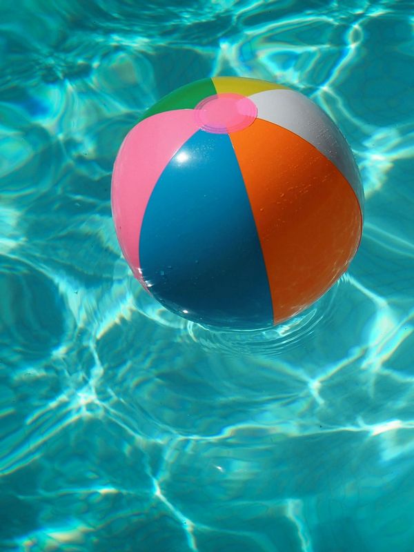 Colorful beach ball floats on clear blue pool water.