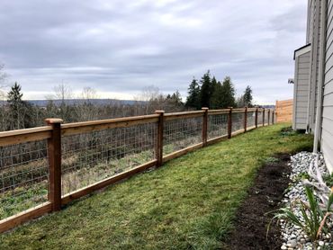 Long wooden fence with wire mesh in a backyard under a cloudy sky.