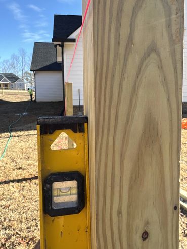 A yellow level tool against a wooden post with a pink string line in outdoor construction.