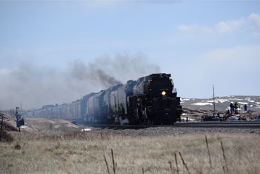 A steam locomotive train emitting smoke travels through a rural landscape.